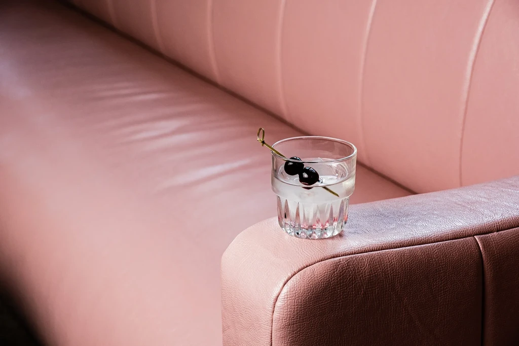 Cocktail with ice and berries on a pick, on a pink armrest.
