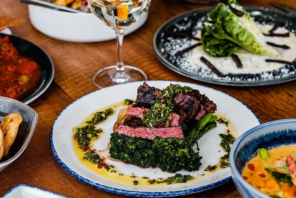 Steak with chimichurri and broccolini on a wooden table.