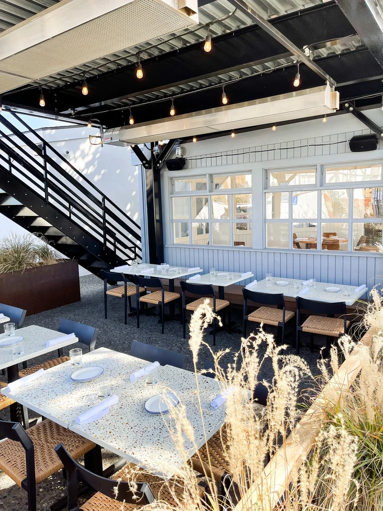 Restaurant patio with pre-set tables, string lights, and modern industrial decor.