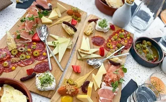 Two wooden boards laden with charcuterie, cheeses, fruit, and vegetables.