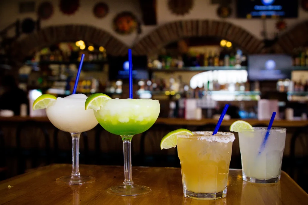 Four varied drinks with garnishes on a wooden table in a bar.