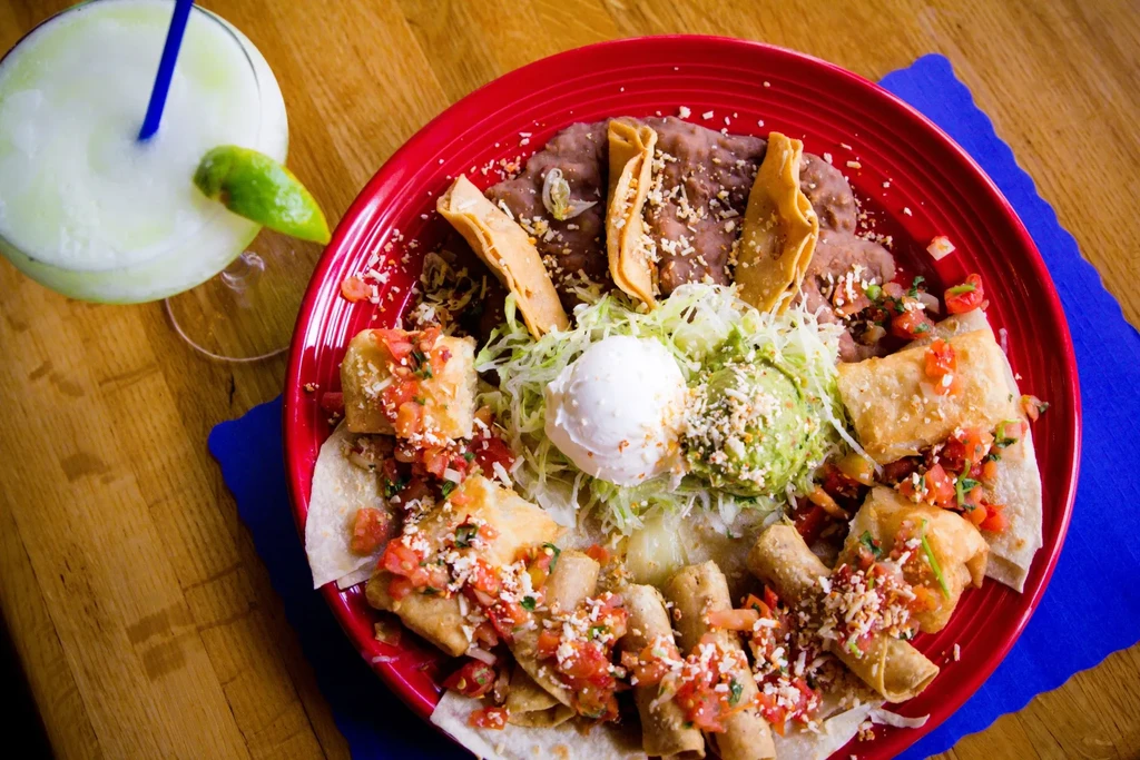 Overhead: Mexican food platter with taquitos, beans, guacamole, margarita.