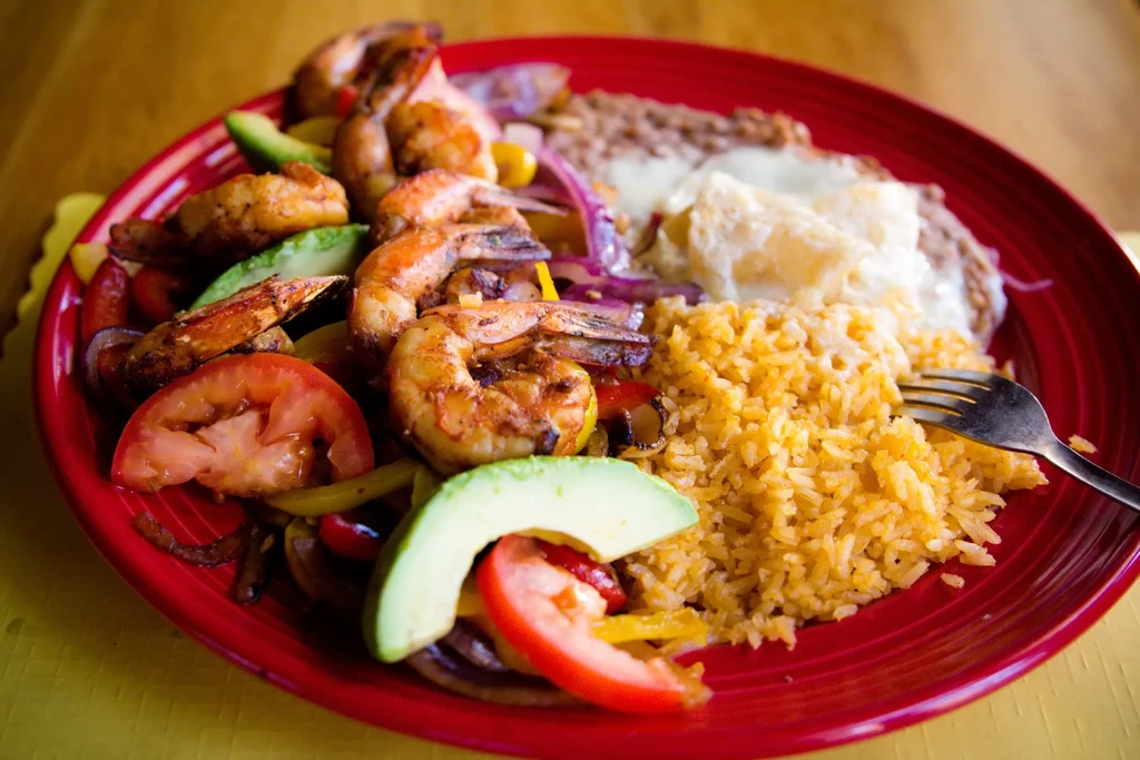Mexican shrimp dish with avocado, tomato, rice, beans on a red plate.