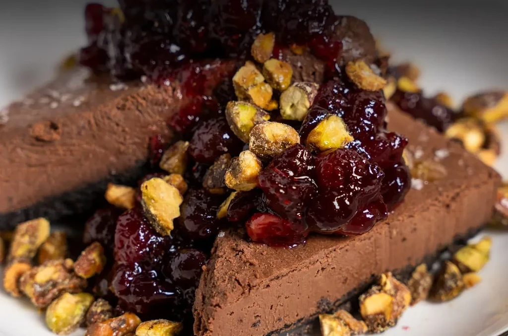 Dark chocolate dessert slices topped with red fruit and pistachios.