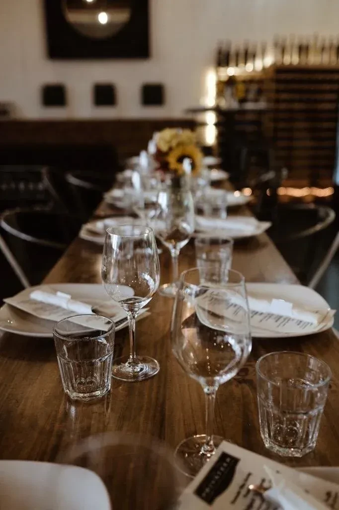 Elegant wooden table set for event with glasses, plates, and sunflowers.
