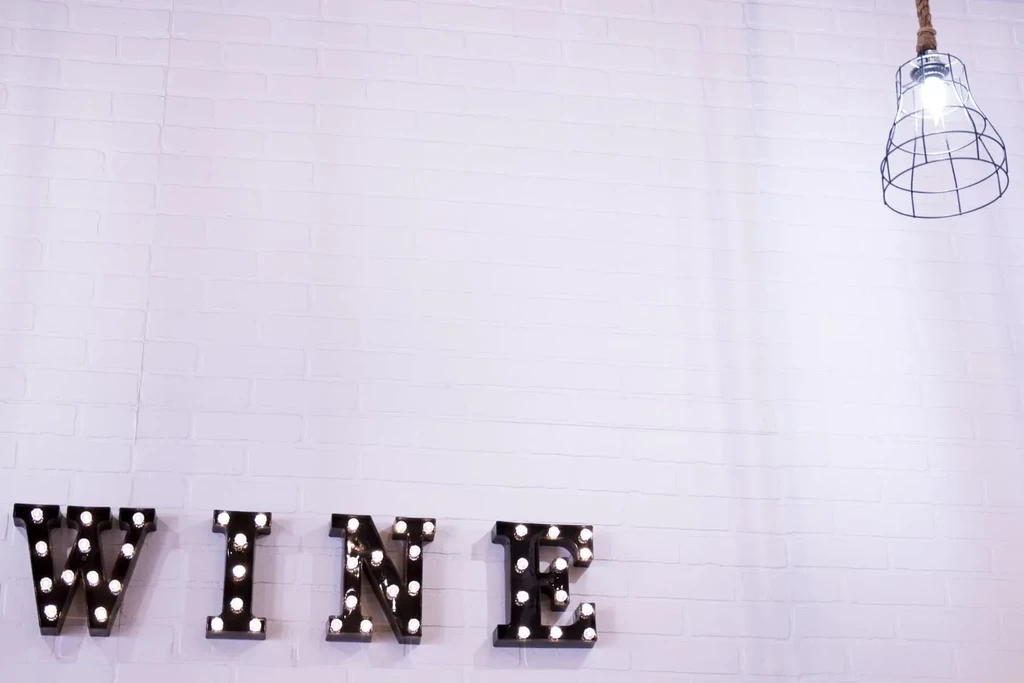 Illuminated 'WINE' sign on white brick wall, industrial light fixture.