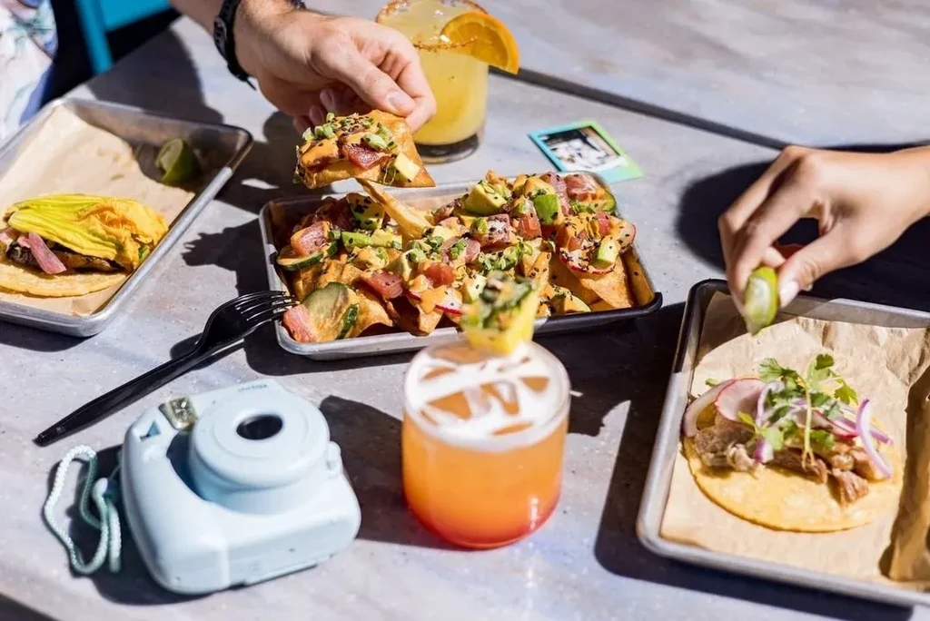 Overhead: Loaded tuna poke nachos, two tacos, cocktails, and an Instax camera.