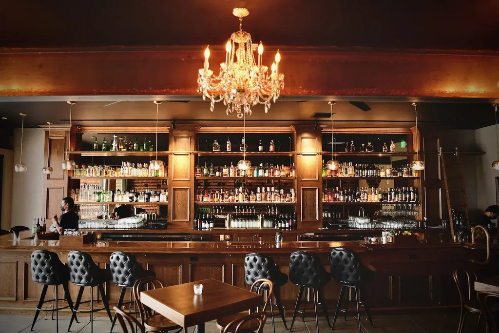 Elegant wooden bar, well-stocked with liquor, beneath a crystal chandelier.