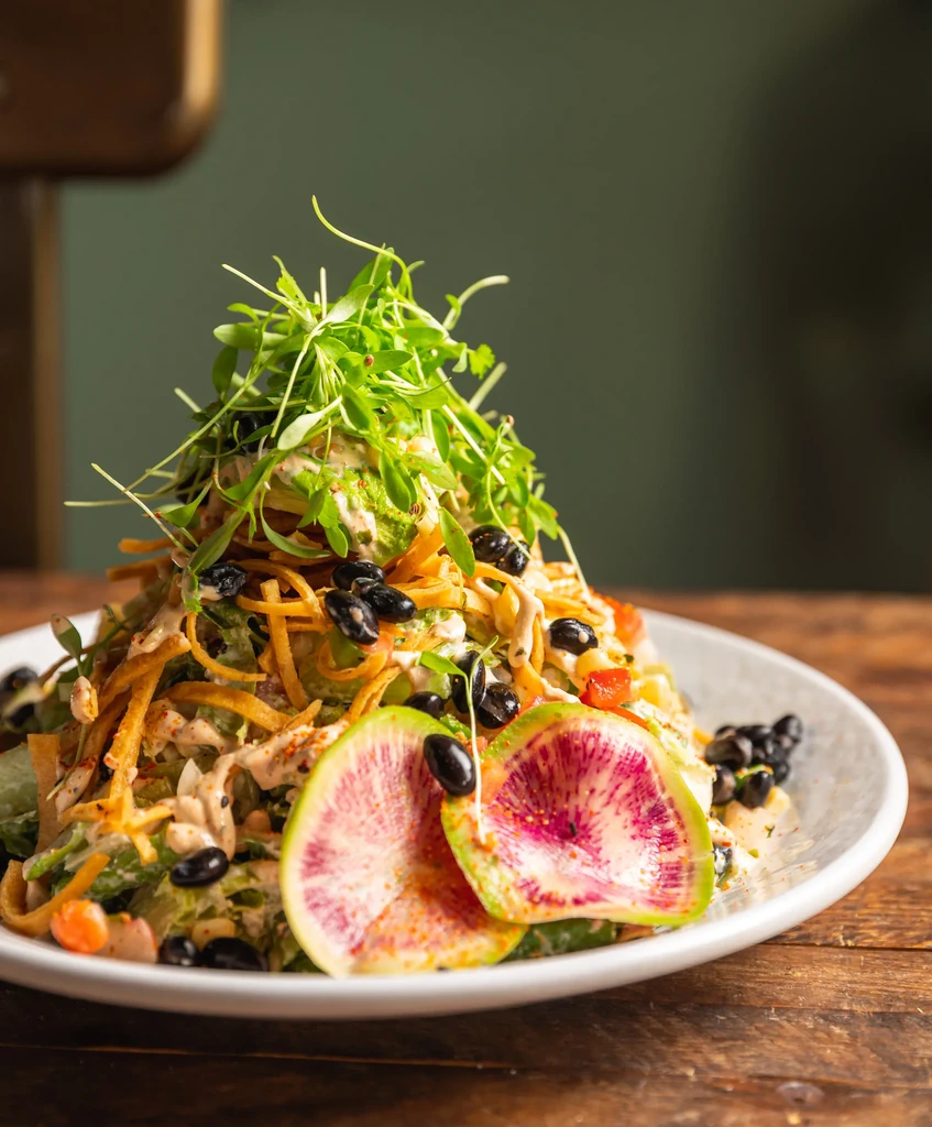 Vibrantly plated salad with microgreens, black beans, watermelon radishes, and dressing.
