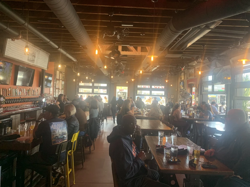Bustling modern industrial-chic restaurant with long bar and many customers.