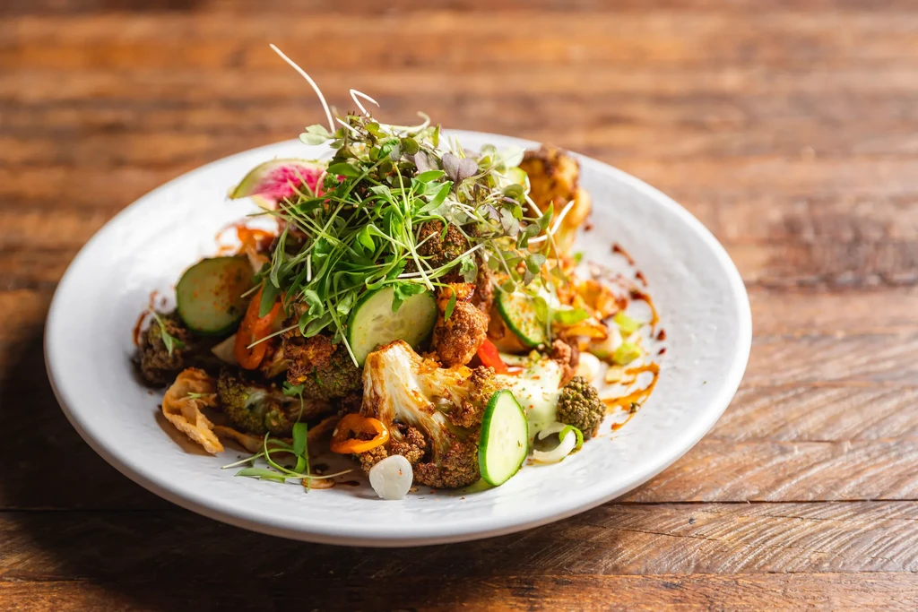 Artfully plated roasted vegetables, pickled radish, microgreens on a white plate.