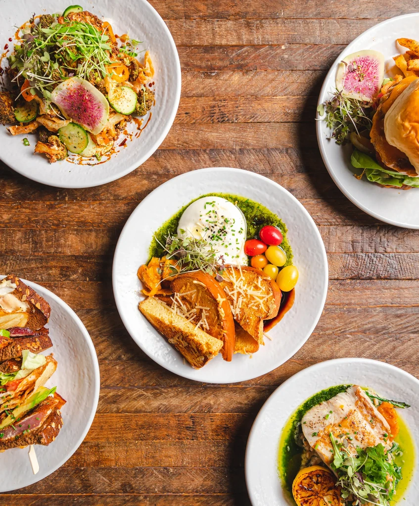 Overhead shot of five diverse, gourmet dishes on a rustic wooden table.
