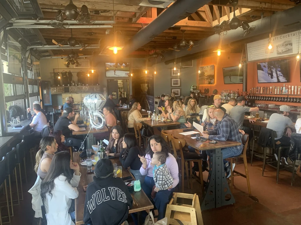 Bustling industrial-rustic restaurant interior with patrons and a '50' balloon.