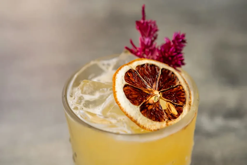 Close-up of pale yellow cocktail with dried orange and magenta flowers.