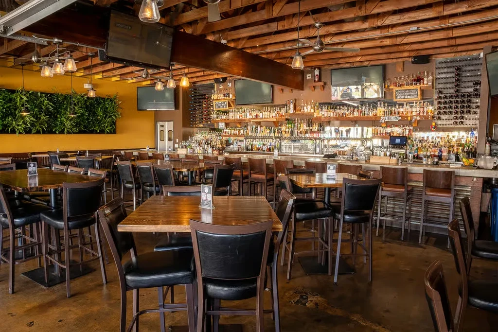 Contemporary bar interior features high-top tables, green wall, and large stocked bar.