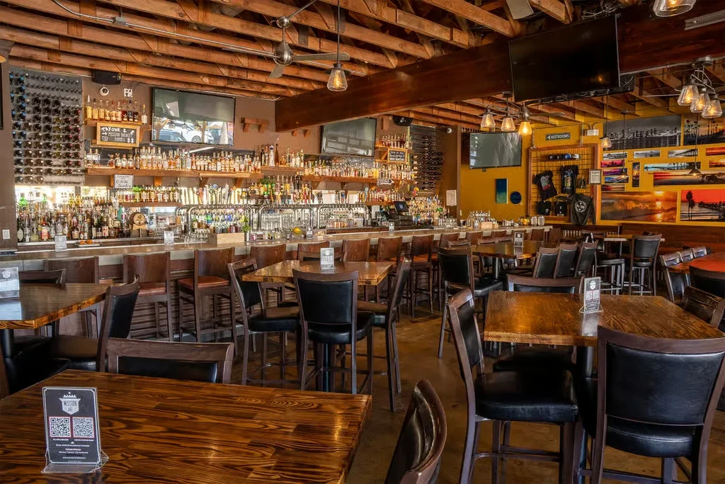 Spacious bar interior with long stocked bar and high-top tables.
