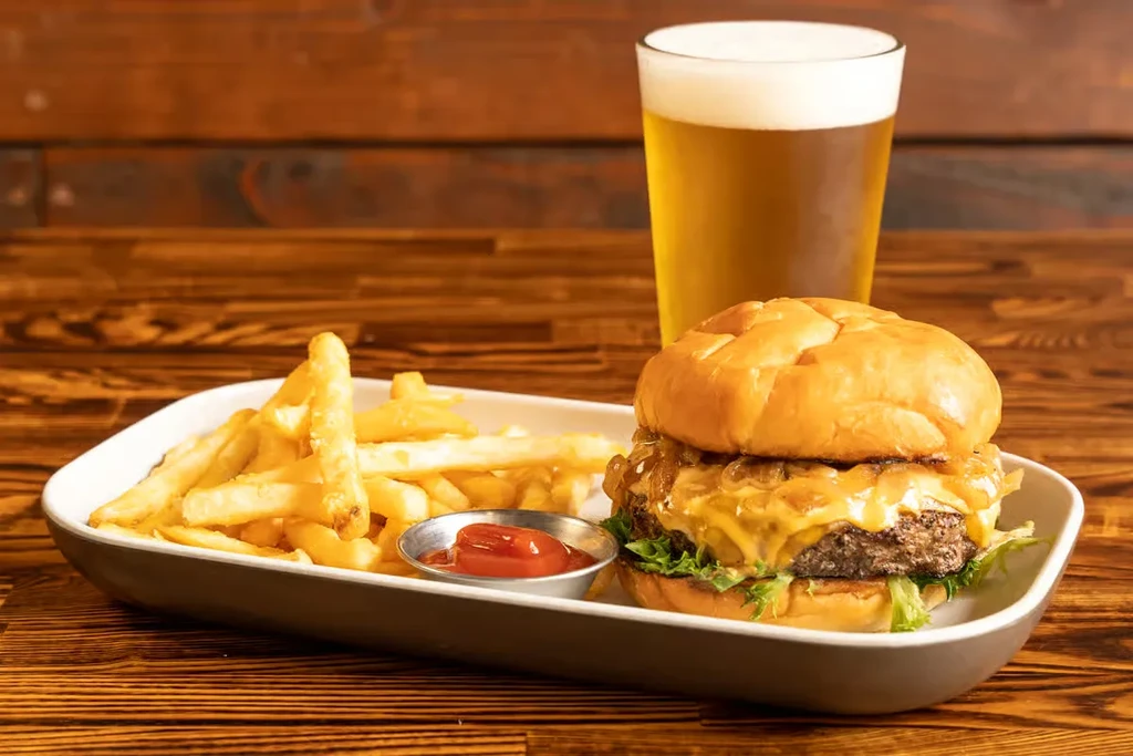 Gourmet burger, french fries, ketchup, and beer on a wooden table.