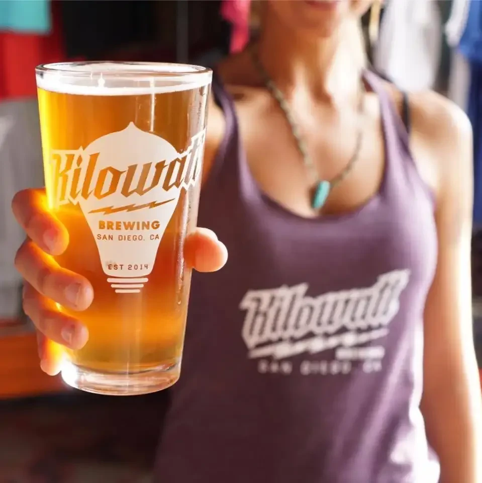 Hand holds Kilowatt Brewing pint glass of golden beer.