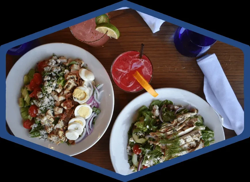 Overhead shot of two salads and two cocktails on a wooden table.