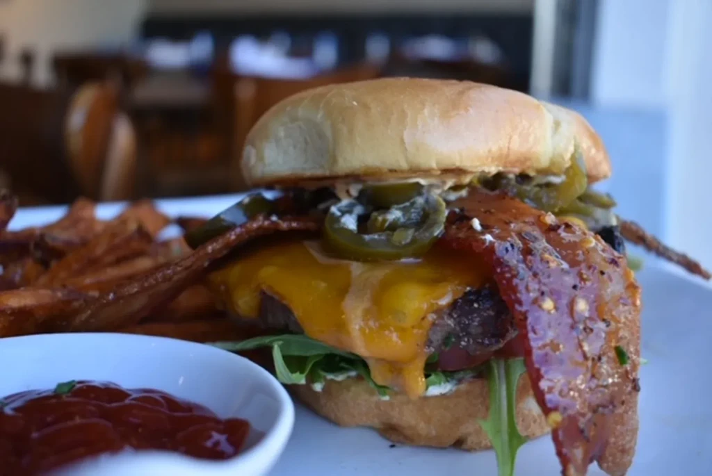 Burger with melted cheddar, bacon, jalapeños, lettuce, tomato, and fries.