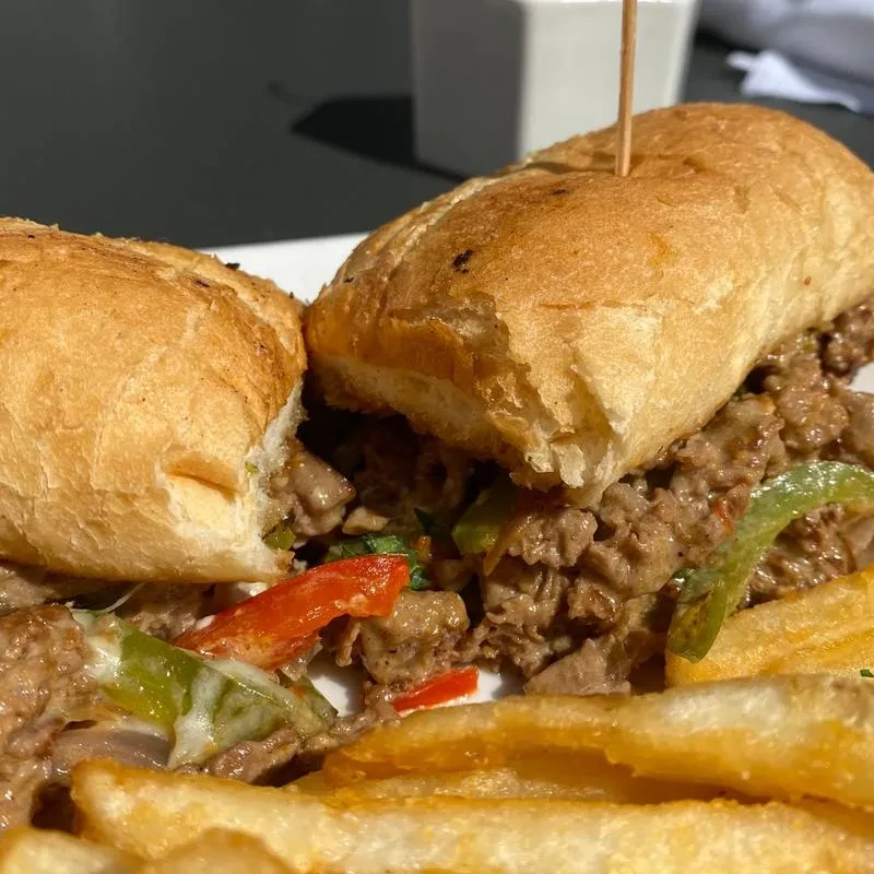 Cheesesteak sandwich with meat, melted cheese, bell peppers, and french fries.