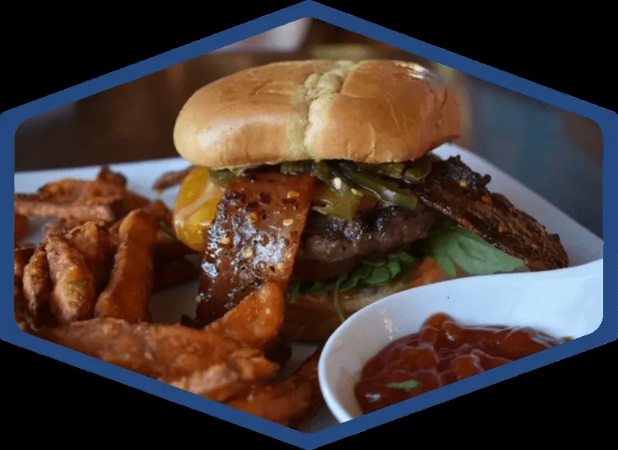 Gourmet burger with bacon, jalapeños, sweet potato fries, and ketchup.