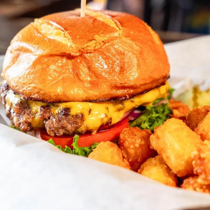 A cheeseburger with melted cheese and crispy tater tots in a container.