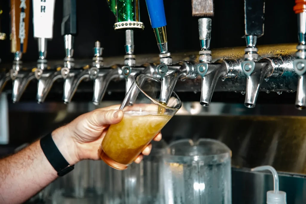 A hand fills a glass of golden beer from a chrome tap.