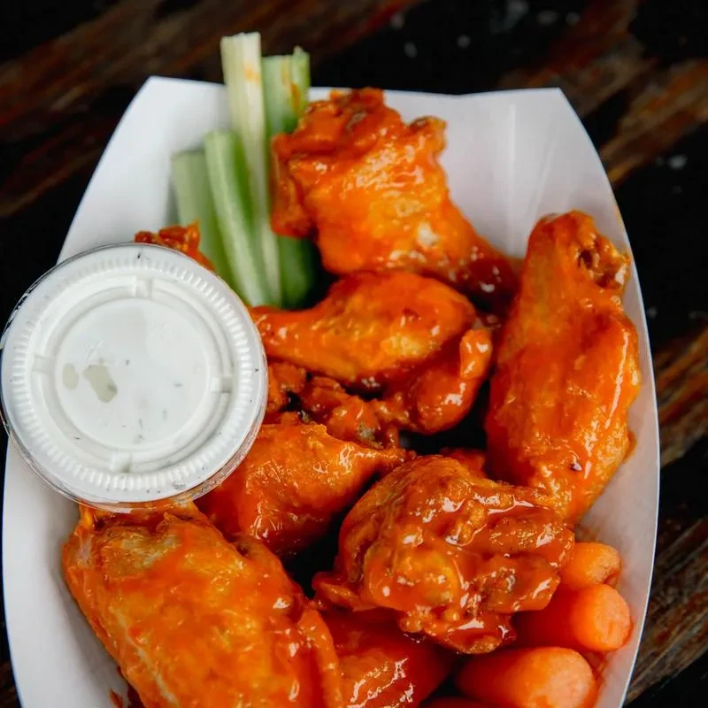 Orange buffalo wings, celery, carrots, and a creamy white dip.