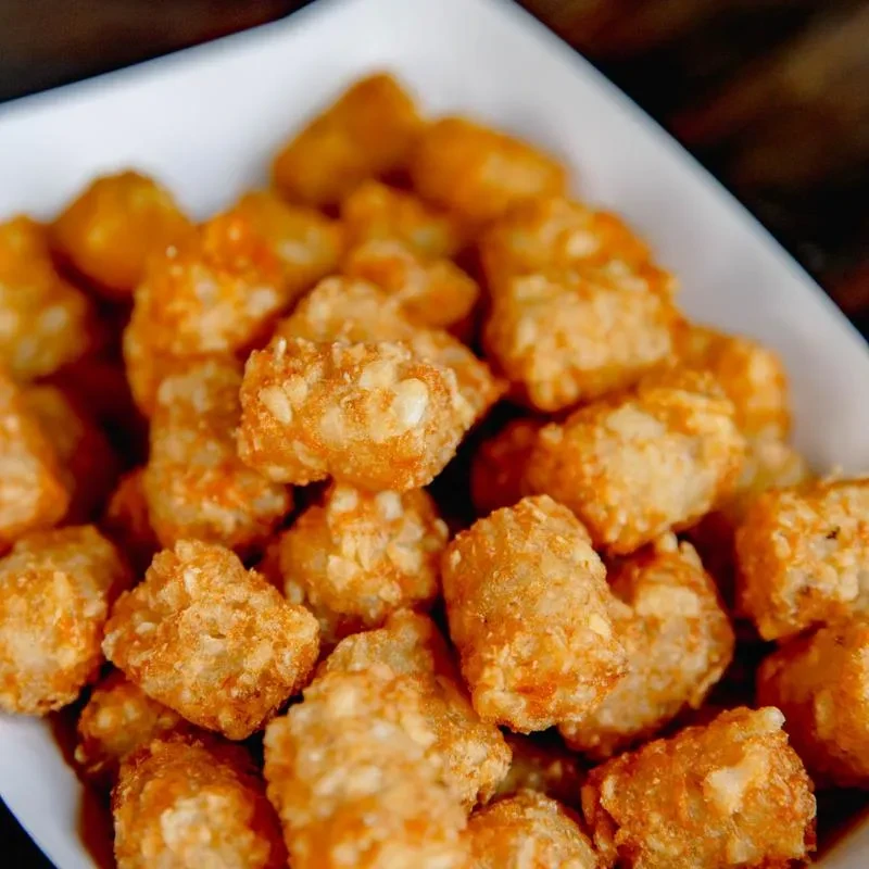 Crispy, golden-brown tater tots piled in a white square dish.