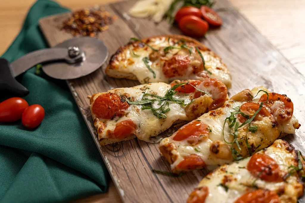 Freshly baked pizza slices with cheese, tomatoes, herbs on rustic wood.