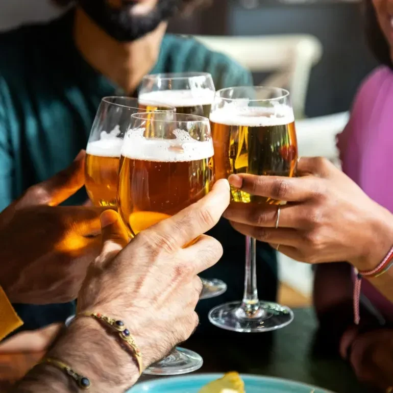 Four hands clinking stemmed beer glasses in a toast.