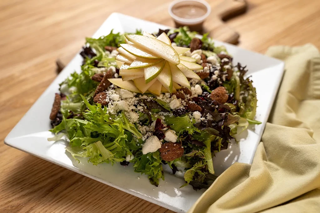 Fresh salad with greens, pears, cheese, cranberries, dressing on wood table.