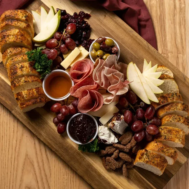 Abundant charcuterie board with cheeses, meats, fruit, bread, and dips.