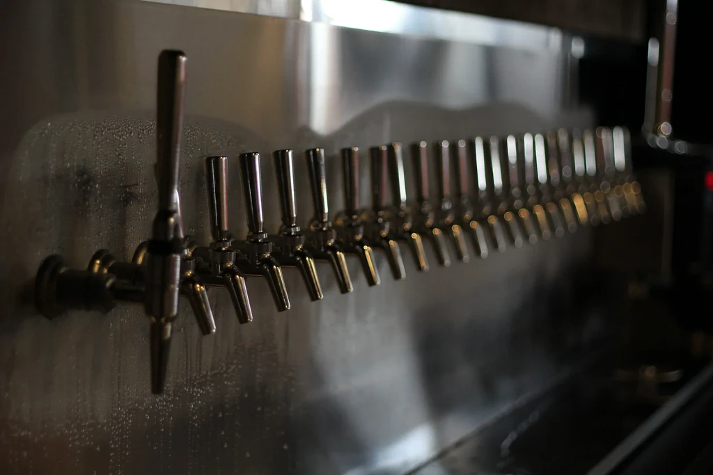 Long line of reflective beer taps with condensation, blurring to the right.