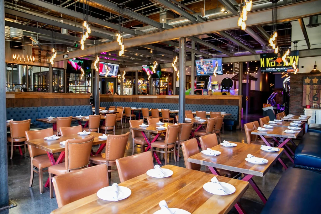Modern industrial-chic restaurant interior with blue booths, leather chairs, and TVs.
