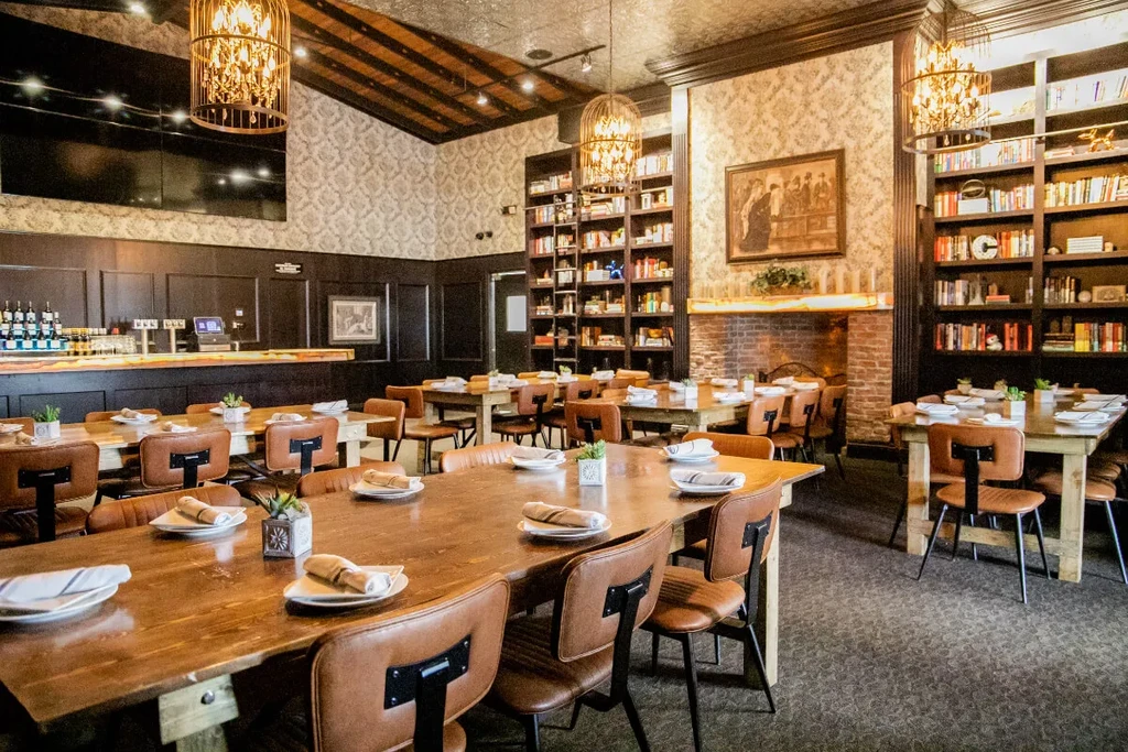 Rustic restaurant interior with wooden tables, fireplace, bookshelves, and bar.