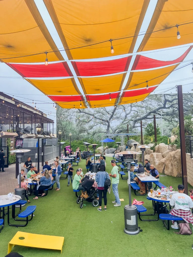 Outdoor dining area under red-yellow canopy, green turf, people dining.