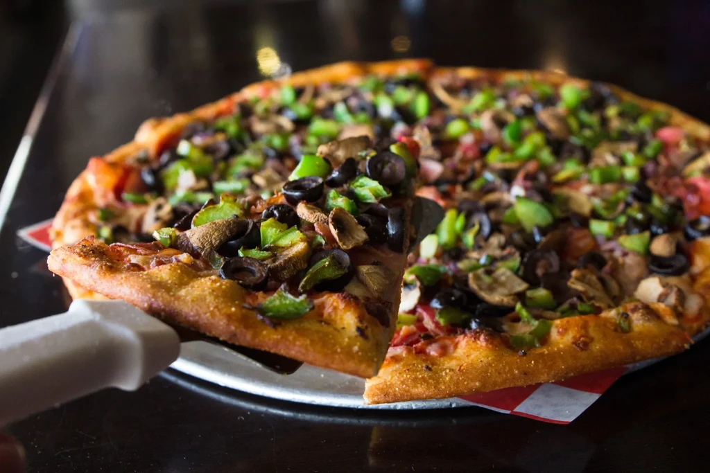 Pizza topped with olives, peppers, mushrooms; one slice being lifted.