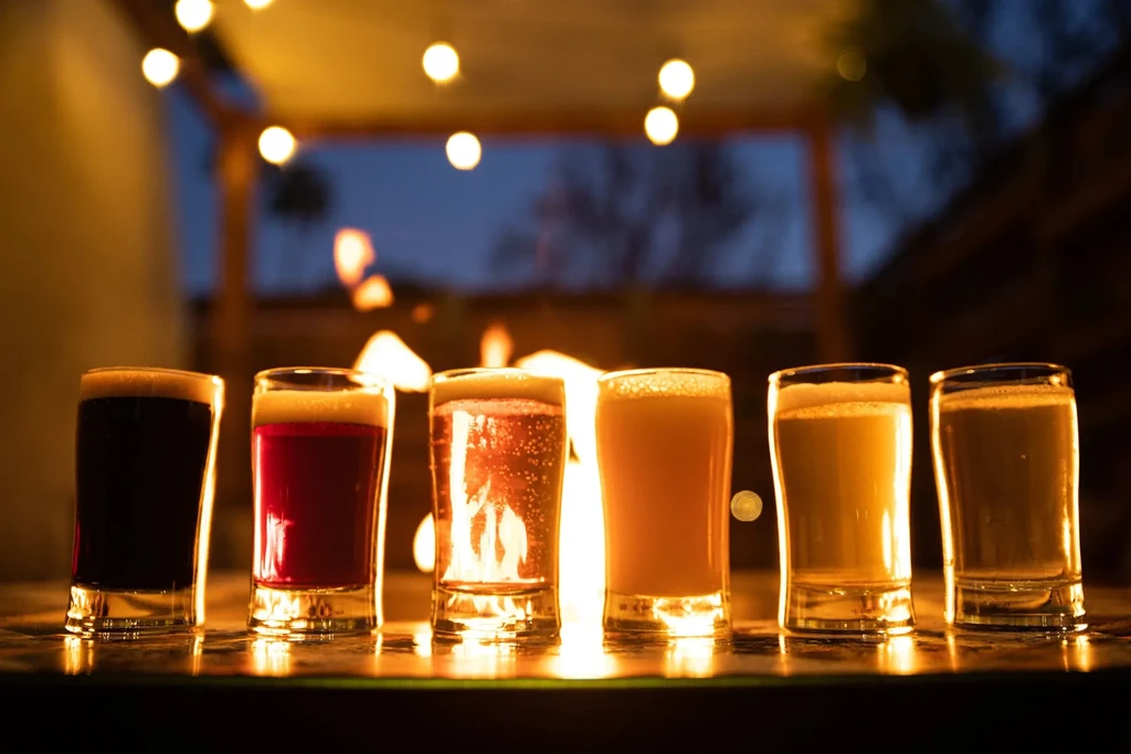 Six diverse drinks, dark to light, in glasses with warm backlighting.
