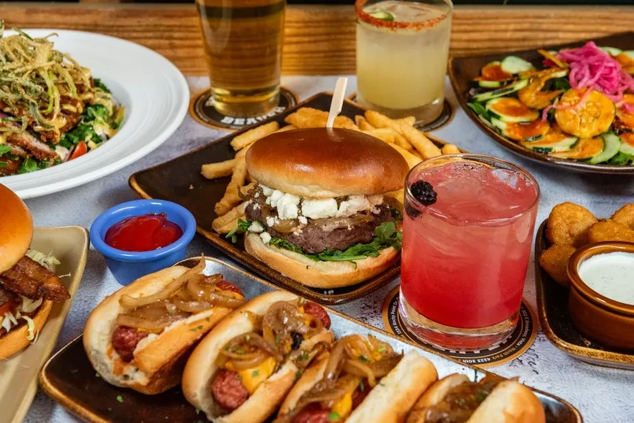 Spread of burger, hot dogs, salads, appetizers, beer, and cocktails.