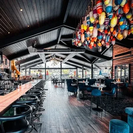 Modern restaurant interior with bar, blue seating, and unique buoy chandelier.
