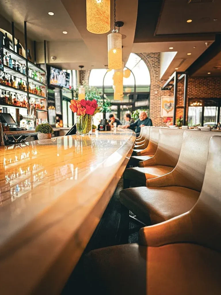 Modern bar interior with wooden counter, tulips, stools, and patrons.