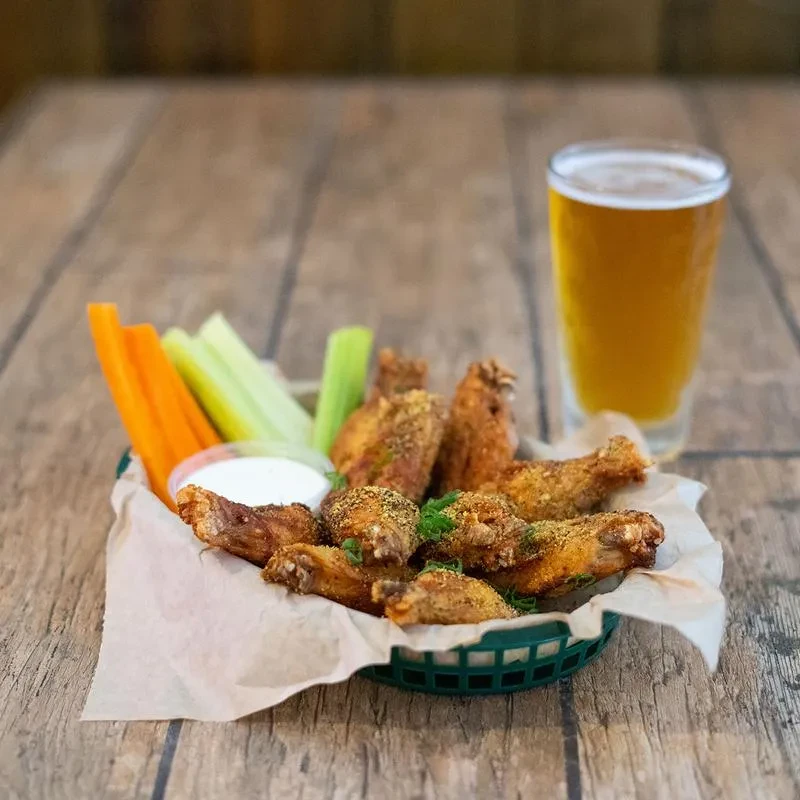Crispy fried chicken wings, veggies, dipping sauce, and beer on a rustic table.