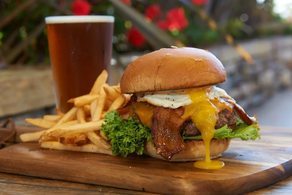Burger with runny fried egg, bacon, fries, and beer.