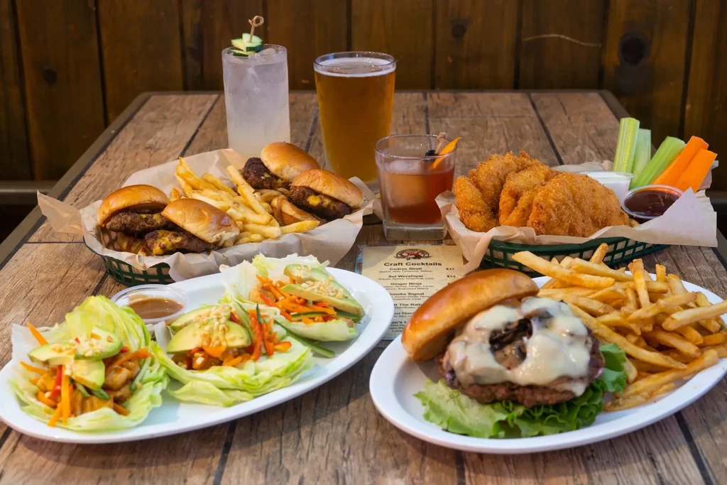 Rustic table with burgers, sliders, wraps, fries, beer, and cocktails.