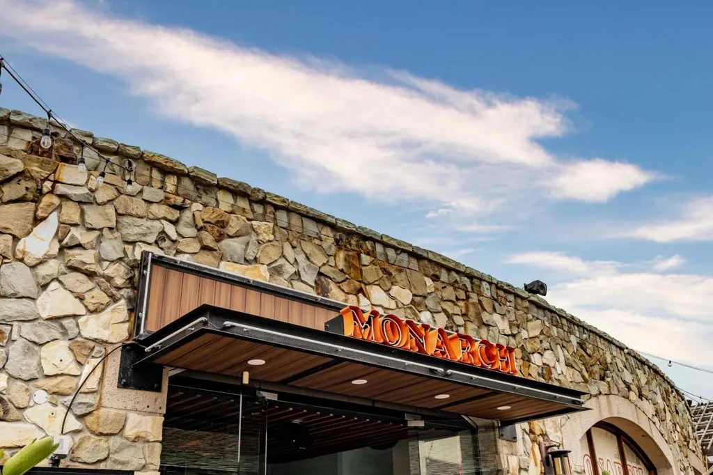 Stone building facade with a modern entrance and "MONARCH" neon sign.