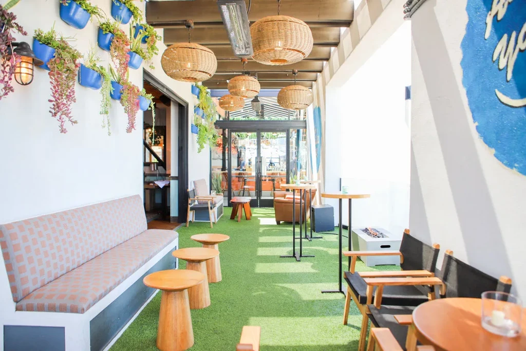 Bright outdoor restaurant patio with plants, artificial grass, and various seating.