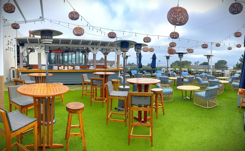 Monarch rooftop bar patio, green turf, string lights, coastal view.