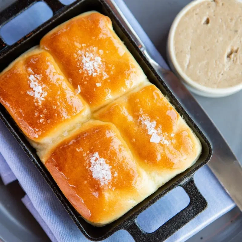Four golden-brown dinner rolls with sea salt in a cast iron pan.